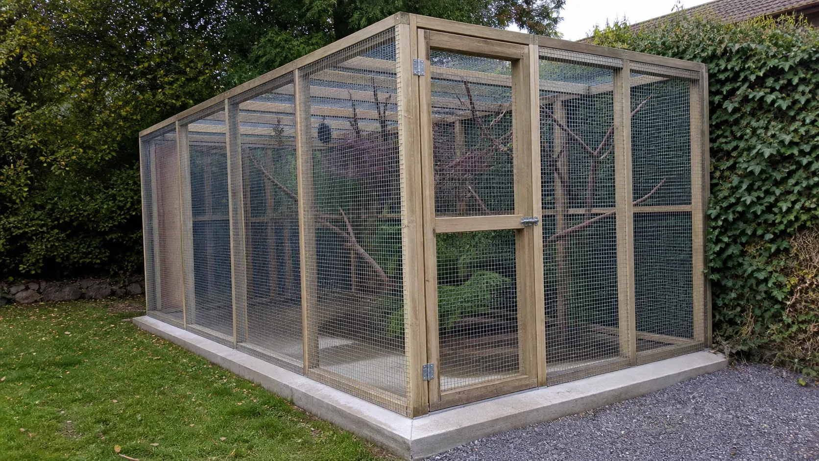 Large outdoor bird aviary securely fixed to a clean concrete base
