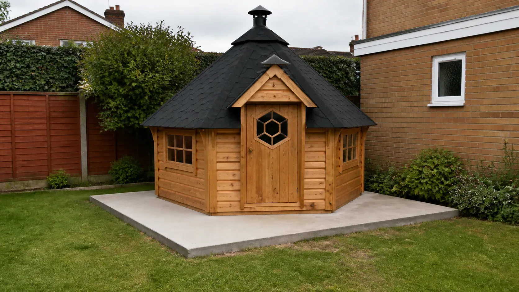 Hexagonal timber BBQ hut in a garden with a neat base