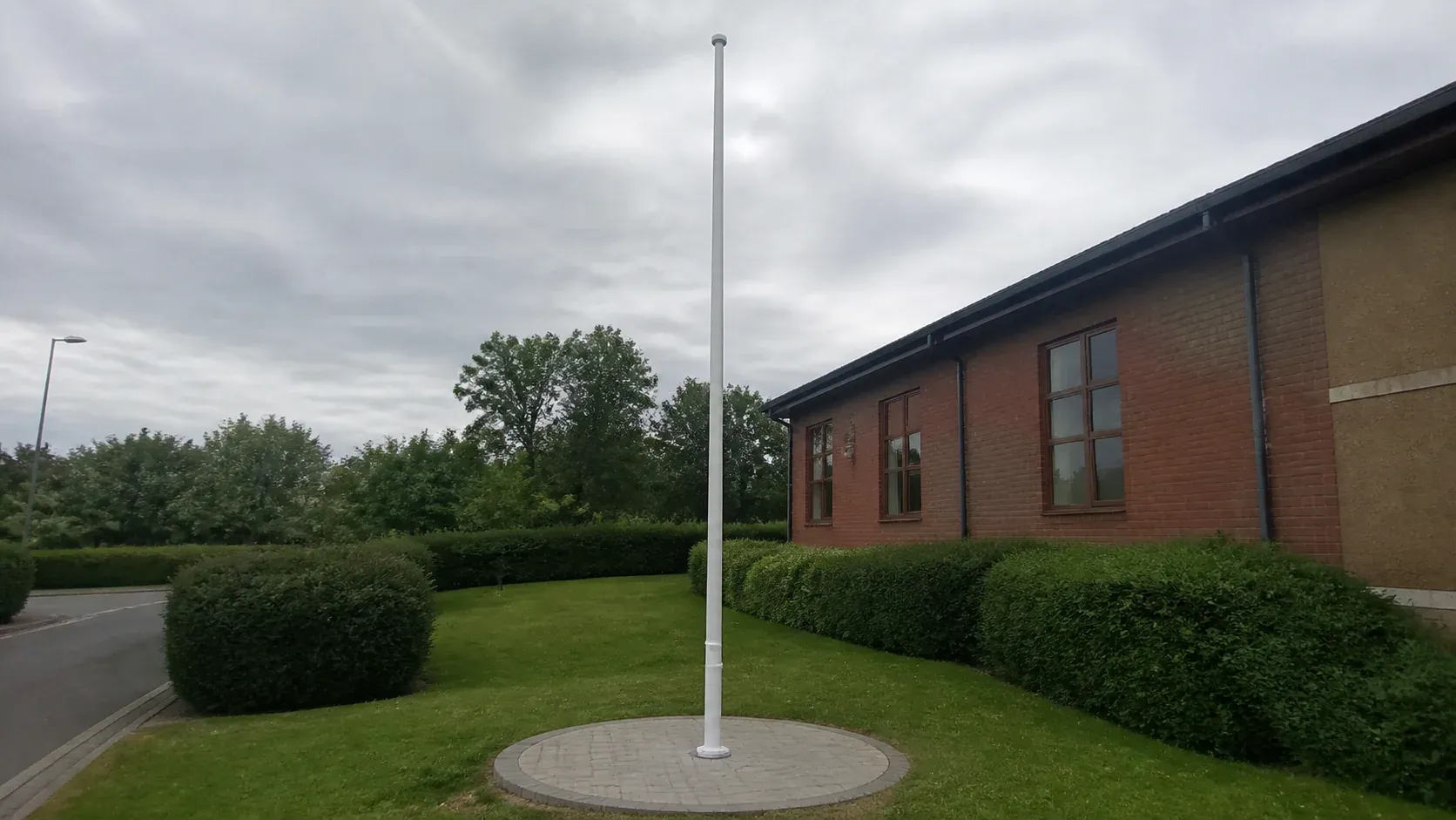 Tall flagpole mounted on a neat concrete foundation in landscaped grounds