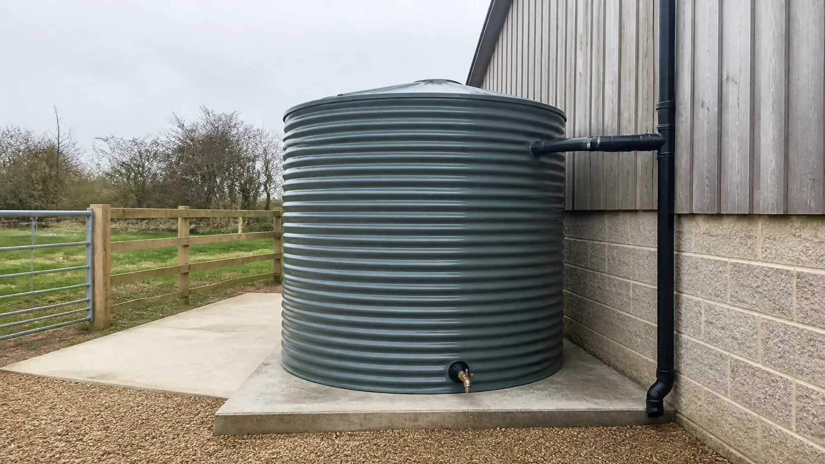 Large rainwater storage tank supported on a level base beside a building