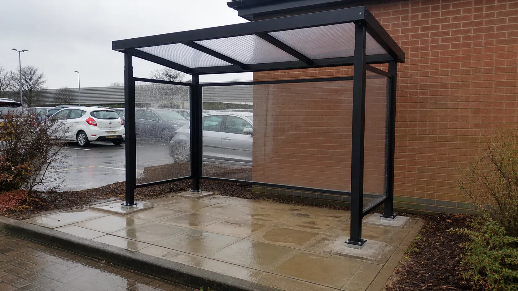 Open-sided workplace smoking shelter securely fixed to a concrete base